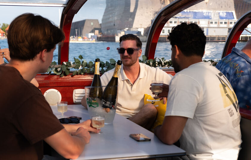 Unge mennesker på Kanalrundfart i København, nyder et koldt glas vin på turen