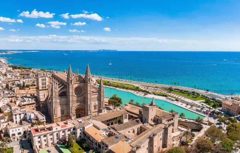 Billedet viser en storslået udsigt over Palma de Mallorca med den ikoniske katedral (La Seu) og Almudaina-paladset i forgrunden ud mod Middelhavet.