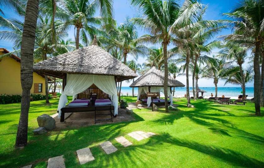 Udendørs spapavilloner på det grønne græs under palmetræerne ved Pandanus Resort i Mũi Né i Vietnam.